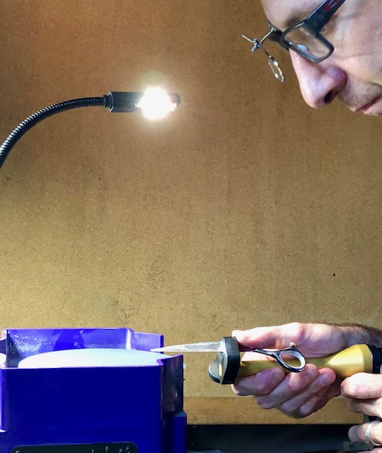 Drew under a bench lamp, checking the edge of a pair of shears