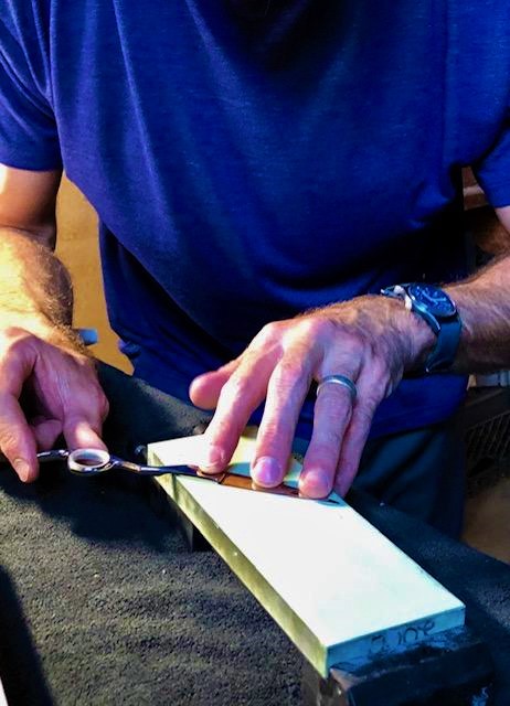 Drew holding a pair of stylist shears flat against a pale water stone